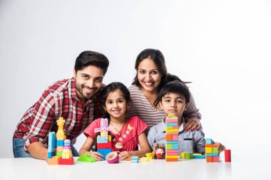 Hintli küçük çocuklar beyaz arka plana karşı genç ebeveynleriyle renkli blok oyuncakları oynuyorlar.