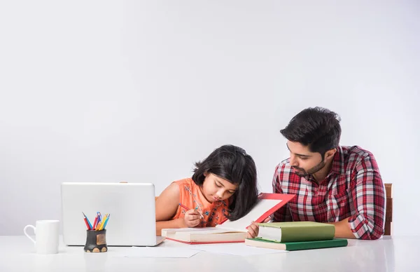 Cute Indian girl with father studying or doing homework at home using laptop and books - online schooling concept