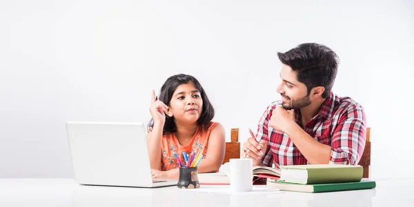 Cute Indian girl with father studying or doing homework at home using laptop and books - online schooling concept