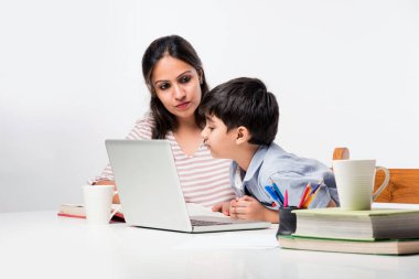 Evde ev ödevi yapan sevimli Hintli çocuk dizüstü bilgisayar ve kitap kullanıyor - online eğitim kavramı.