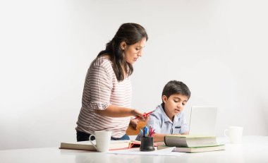 Evde ev ödevi yapan sevimli Hintli çocuk dizüstü bilgisayar ve kitap kullanıyor - online eğitim kavramı.