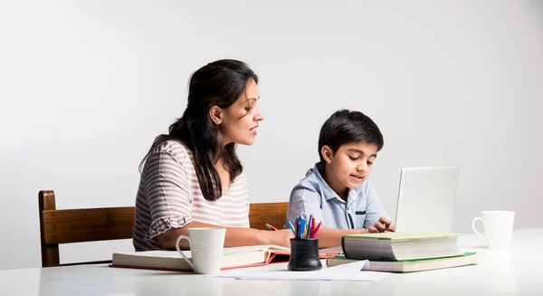 Cute Indian boy with mother doing homework at home using laptop and books - online schooling concept