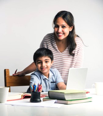 Evde ev ödevi yapan sevimli Hintli çocuk dizüstü bilgisayar ve kitap kullanıyor - online eğitim kavramı.