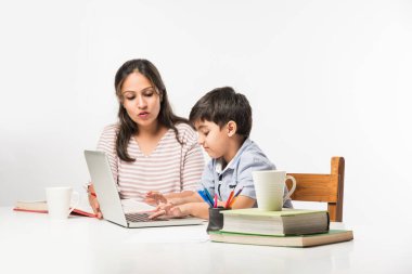 Evde ev ödevi yapan sevimli Hintli çocuk dizüstü bilgisayar ve kitap kullanıyor - online eğitim kavramı.