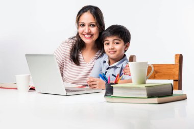 Evde ev ödevi yapan sevimli Hintli çocuk dizüstü bilgisayar ve kitap kullanıyor - online eğitim kavramı.