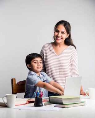 Evde ev ödevi yapan sevimli Hintli çocuk dizüstü bilgisayar ve kitap kullanıyor - online eğitim kavramı.