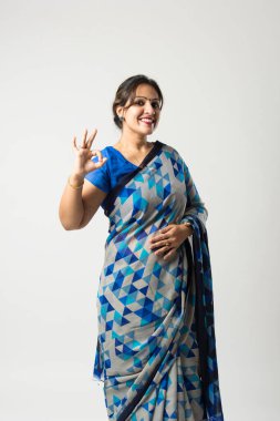 Sari ya da sari giymiş başarılı bir Hintli genç kadın portresi, elleri katlı ya da baş parmakları yukarıda, beyaz arka planda izole edilmiş.