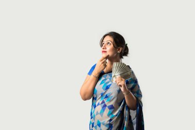 Sari ya da sari giymiş Hintli bir kadın beyaz arka planda kağıt para ya da para fanı gösteriyor ya da tutuyor.