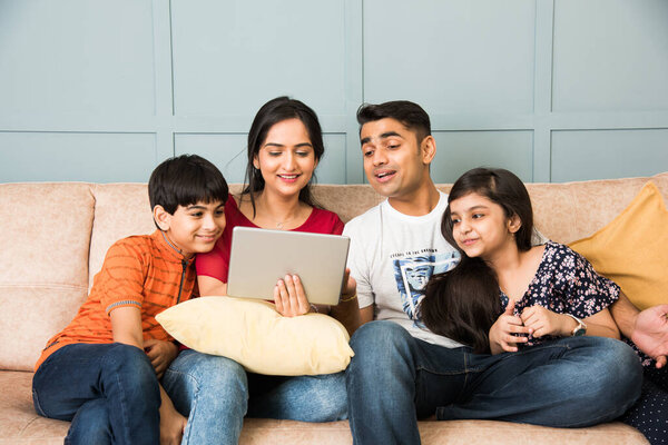Индийская семья сидит на диване и с помощью смартфона, ноутбука или планшета, смотреть кино или серфинг Интернет