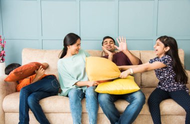 Hint ailesi kanepe ya da kanepede yastık savaşı yapıyor. Ebeveynler boş zamanlarını küçük çocuklarıyla geçirirler.