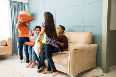 Hint ailesi kanepe ya da kanepede yastık savaşı yapıyor. Ebeveynler boş zamanlarını küçük çocuklarıyla geçirirler.