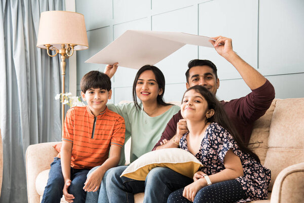 Индийская семья Отец, мать, сын и дочь держат дом крышу из картона - Real Istate Concept в Индии