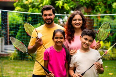 Hindistan 'ın küçük erkek kardeşi açık alanda badminton oynuyor, Asyalı küçük kardeşler gündüz vakti mekik ve raketle eğleniyor, aktif çocukluk anı.