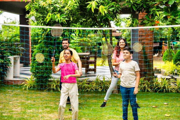 Hindistan 'ın küçük erkek kardeşi açık alanda badminton oynuyor, Asyalı küçük kardeşler gündüz vakti mekik ve raketle eğleniyor, aktif çocukluk anı.