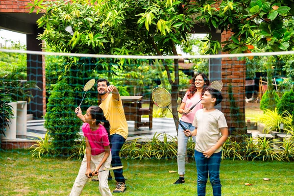 Hindistan 'ın küçük erkek kardeşi açık alanda badminton oynuyor, Asyalı küçük kardeşler gündüz vakti mekik ve raketle eğleniyor, aktif çocukluk anı.