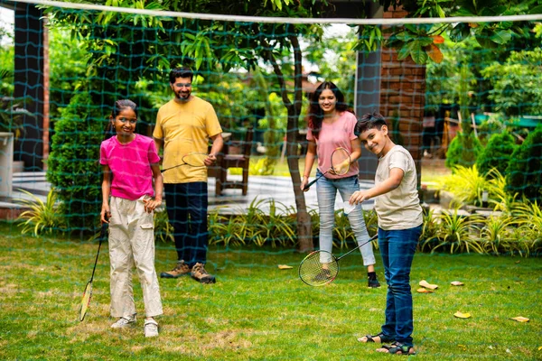 Hindistan 'ın küçük erkek kardeşi açık alanda badminton oynuyor, Asyalı küçük kardeşler gündüz vakti mekik ve raketle eğleniyor, aktif çocukluk anı.