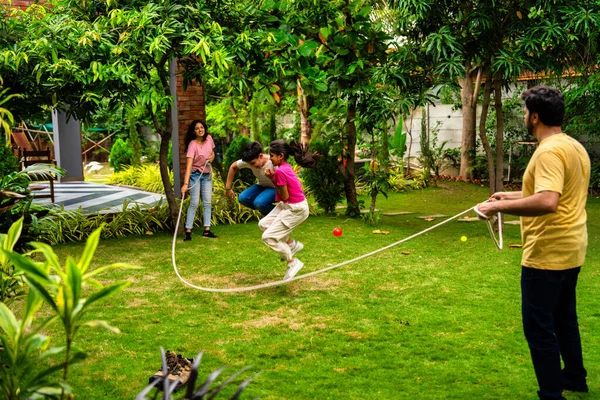 Ev bahçesinde ip atlama oyunu oynayan Hintli bir aile. Birlikte güzel vakit geçiriyorlar. Açık hava sporlarının tadını çıkarıyorlar.