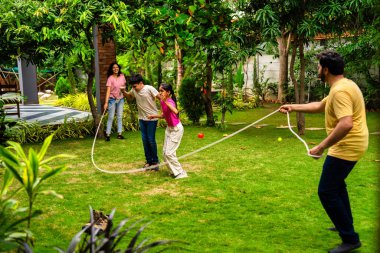Ev bahçesinde ip atlama oyunu oynayan Hintli bir aile. Birlikte güzel vakit geçiriyorlar. Açık hava sporlarının tadını çıkarıyorlar.