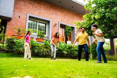 Ev bahçesinde göz kapağı oyunu oynayan Hintli aile, birlikte güzel vakit geçiriyorlar. Açık hava sporlarının tadını çıkarıyorlar. Ebeveynler ve çocuklar gülüyor, koşuyor ve oyuncu arka bahçe aktiviteleriyle kaynaşıyorlar.