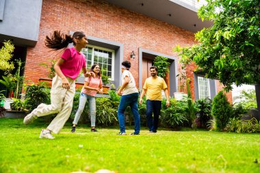 Ev bahçesinde göz kapağı oyunu oynayan Hintli aile, birlikte güzel vakit geçiriyorlar. Açık hava sporlarının tadını çıkarıyorlar. Ebeveynler ve çocuklar gülüyor, koşuyor ve oyuncu arka bahçe aktiviteleriyle kaynaşıyorlar.