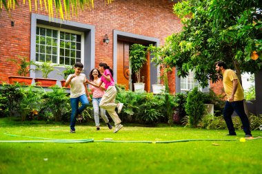 Ev bahçesinde Langdi oyunu oynayan Hintli bir aile, açık hava sporlarından zevk alarak birlikte kaliteli zaman geçiriyorlar, geleneksel Hint takım oyununda tek ayak üzerinde zıplayıp çeviklik tabanlı oyunu birleştiriyorlar.