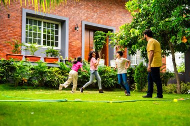 Ev bahçesinde Langdi oyunu oynayan Hintli bir aile, açık hava sporlarından zevk alarak birlikte kaliteli zaman geçiriyorlar, geleneksel Hint takım oyununda tek ayak üzerinde zıplayıp çeviklik tabanlı oyunu birleştiriyorlar.