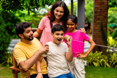 Ev bahçesinde telli telefonla oynayan Hintli aile, dışarıda yaratıcı aktivitelerden zevk alıyor, çocuklarla, ebeveynlerle, kardeşlerle eğlenceli vakit geçiriyor, gülümsüyor ve neşeyle kaynaşıyor.