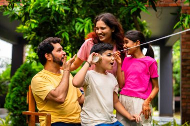 Ev bahçesinde telli telefonla oynayan Hintli aile, dışarıda yaratıcı aktivitelerden zevk alıyor, çocuklarla, ebeveynlerle, kardeşlerle eğlenceli vakit geçiriyor, gülümsüyor ve neşeyle kaynaşıyor.