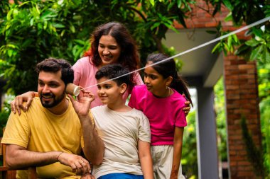 Ev bahçesinde telli telefonla oynayan Hintli aile, dışarıda yaratıcı aktivitelerden zevk alıyor, çocuklarla, ebeveynlerle, kardeşlerle eğlenceli vakit geçiriyor, gülümsüyor ve neşeyle kaynaşıyor.