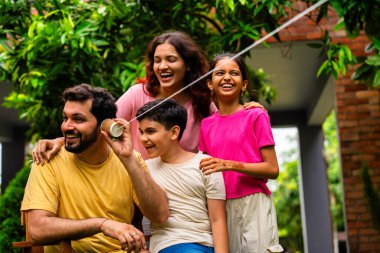 Ev bahçesinde telli telefonla oynayan Hintli aile, dışarıda yaratıcı aktivitelerden zevk alıyor, çocuklarla, ebeveynlerle, kardeşlerle eğlenceli vakit geçiriyor, gülümsüyor ve neşeyle kaynaşıyor.