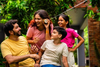 Ev bahçesinde telli telefonla oynayan Hintli aile, dışarıda yaratıcı aktivitelerden zevk alıyor, çocuklarla, ebeveynlerle, kardeşlerle eğlenceli vakit geçiriyor, gülümsüyor ve neşeyle kaynaşıyor.
