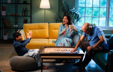 Hintli çocuk modern evde büyükanne ve büyükbabasıyla carrom oynuyor. Yaşlı büyükanne ve büyükbaba çocuklarla oyun oynuyor. Aile bağları, geleneksel Hint yaşam tarzı, eğlence, neşe.