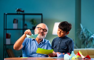 Hintli büyükbaba ve çocuk evde kağıt işleriyle uğraşıyorlar, renkli tekne ve uçakları parlak kağıtlarla eğitiyorlar, yaşlı adam torununa yaratıcı aktiviteler öğretiyor, aile içi bağlar kuruyor.