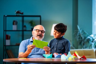 Hintli büyükbaba ve çocuk evde kağıt işleriyle uğraşıyorlar, renkli tekne ve uçakları parlak kağıtlarla eğitiyorlar, yaşlı adam torununa yaratıcı aktiviteler öğretiyor, aile içi bağlar kuruyor.