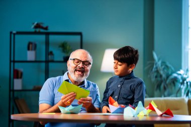 Hintli büyükbaba ve çocuk evde kağıt işleriyle uğraşıyorlar, renkli tekne ve uçakları parlak kağıtlarla eğitiyorlar, yaşlı adam torununa yaratıcı aktiviteler öğretiyor, aile içi bağlar kuruyor.