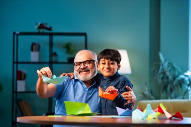 Hintli büyükbaba ve çocuk evde kağıt işleriyle uğraşıyorlar, renkli tekne ve uçakları parlak kağıtlarla eğitiyorlar, yaşlı adam torununa yaratıcı aktiviteler öğretiyor, aile içi bağlar kuruyor.