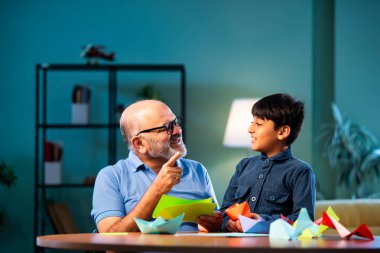 Hintli büyükbaba ve çocuk evde kağıt işleriyle uğraşıyorlar, renkli tekne ve uçakları parlak kağıtlarla eğitiyorlar, yaşlı adam torununa yaratıcı aktiviteler öğretiyor, aile içi bağlar kuruyor.