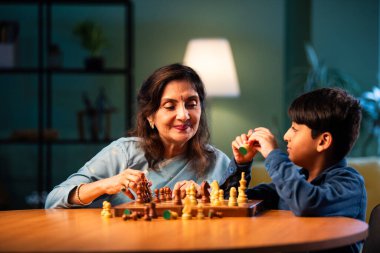 Hintli büyükanne ve çocuk modern evde masada satranç oynuyorlar, yaşlı kadın çocuklara stratejik oyun öğretiyor, aile bağı, zihinsel egzersiz, aşk, sabır, birliktelik