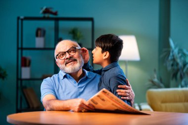 Hintli çocuk, büyükbabasına evde dedikodu yapıyor. Büyükbabası masada otururken sırrını paylaşıyor. Çocuk, evde yaşlı bir adama gizli haberler fısıldıyor.