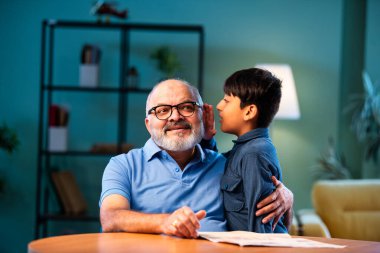 Hintli çocuk, büyükbabasına evde dedikodu yapıyor. Büyükbabası masada otururken sırrını paylaşıyor. Çocuk, evde yaşlı bir adama gizli haberler fısıldıyor.