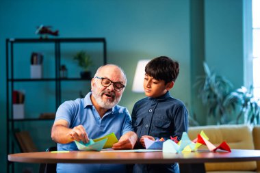 Hintli büyükbaba ve çocuk evde kağıt işleriyle uğraşıyorlar, renkli tekne ve uçakları parlak kağıtlarla eğitiyorlar, yaşlı adam torununa yaratıcı aktiviteler öğretiyor, aile içi bağlar kuruyor.