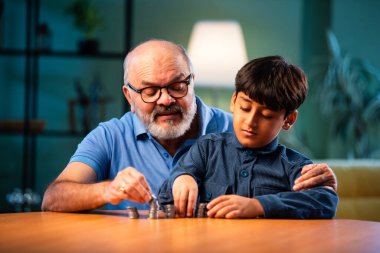 Hintli büyükbaba ve çocuk evde madeni para kulesi yapıyor, yaşlı adam toruna para değerini öğretiyor, daha iyi bir mali gelecek için tasarruf alışkanlığını teşvik ediyor, aile içi bağlılık anı