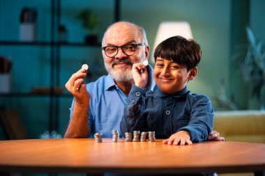 Hintli büyükbaba ve çocuk evde madeni para kulesi yapıyor, yaşlı adam toruna para değerini öğretiyor, daha iyi bir mali gelecek için tasarruf alışkanlığını teşvik ediyor, aile içi bağlılık anı