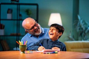 Hintli büyükbaba, çocuklara kalemle resim çizmede ya da boyamada yardım ediyor. İkisi de modern evdeki masada birlikte oturuyor. Yaşlı adam, torununa yaratıcı aktivitelerde rehberlik ediyor.