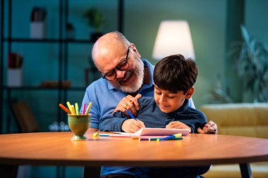 Hintli büyükbaba, çocuklara kalemle resim çizmede ya da boyamada yardım ediyor. İkisi de modern evdeki masada birlikte oturuyor. Yaşlı adam, torununa yaratıcı aktivitelerde rehberlik ediyor.
