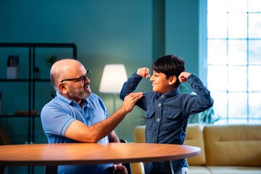 Hintli büyükbaba ve çocuk bilek güreşi yapıyorlar. İkisi de modern evdeki masada birlikte oturuyorlar. Yaşlı adam ve torun eğlenceli aktivitelerin keyfini çıkarıyorlar.