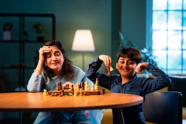 Hintli büyükanne ve çocuk modern evde masada satranç oynuyorlar, yaşlı kadın çocuklara stratejik oyun öğretiyor, aile bağı, zihinsel egzersiz, aşk, sabır, birliktelik