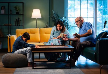 Hintli çocuk modern evde büyükanne ve büyükbabasıyla carrom oynuyor. Yaşlı büyükanne ve büyükbaba çocuklarla oyun oynuyor. Aile bağları, geleneksel Hint yaşam tarzı, eğlence, neşe.