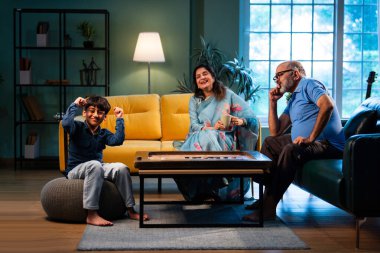 Hintli çocuk modern evde büyükanne ve büyükbabasıyla carrom oynuyor. Yaşlı büyükanne ve büyükbaba çocuklarla oyun oynuyor. Aile bağları, geleneksel Hint yaşam tarzı, eğlence, neşe.