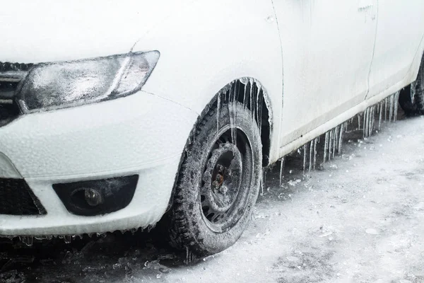 白色冷冻车的侧视特写镜头与冰冻的雨冰柱挂在轮胎停止在一个停车场覆盖在雪冬天的时间 — 图库照片